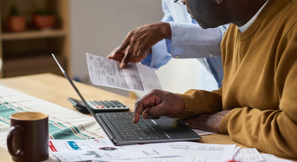 Person reviewing finances at desk with laptop, calculator, notes, looking thoughtful about investment risk decisions.